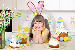 Cute little girl with bunny ears in the kitchen is smiling near the Easter cake