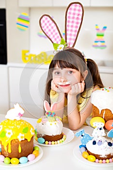 A cute little girl with bunny ears prepares an Easter cake and painted eggs. Religious holiday