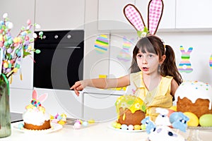 A cute little girl with bunny ears prepares an Easter cake and painted eggs. Religious holiday