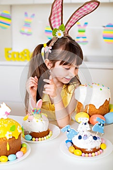 A cute little girl with bunny ears prepares an Easter cake and painted eggs. Religious holiday