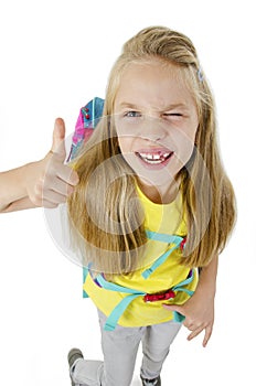 Cute little girl in casual school clothing is showing thumbs up sign. Winking and smiling. Isolated on white background.