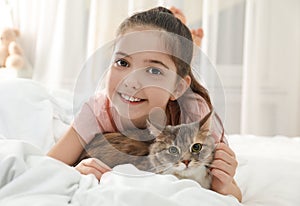 Cute little girl with cat lying on bed. First pet