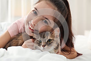 Cute little girl with cat lying on bed at home. First pet