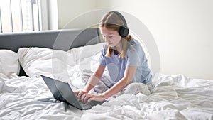 Cute Little Girl Chatting With Friends On Social Media With Laptop On The Bed