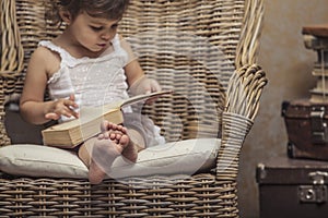 Cute little girl child in a chair, reading a book in interior