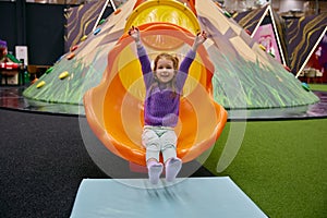 Cute little girl child riding on slide at indoor playground