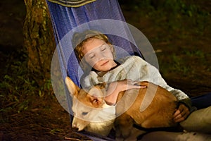 Cute little girl child sleeping in hammock and holding a corgi dog together in camping trip