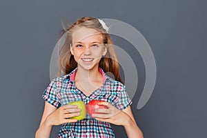 A cute little girl chooses between a green and red Apple on a gray background. The concept of choosing or making a