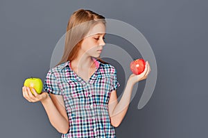 A cute little girl chooses between a green and red Apple on a gray background. The concept of choosing or making a