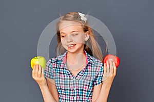 A cute little girl chooses between a green and red Apple on a gray background. The concept of choosing or making a difficult