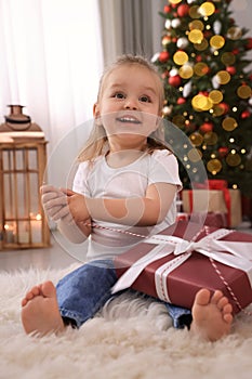 Cute little girl with Christmas gift in festively decorated room