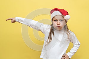 Cute little girl in a Christmas hat. The girl shows emotions on a yellow background. New year concept