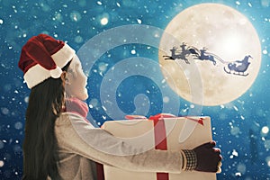 Cute little girl with christmas presents. Santa Claus flying in  moon sky