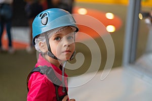 Cute little girl climber in blue protective helmet and gear for climbing standing in climber centre amusement park for children