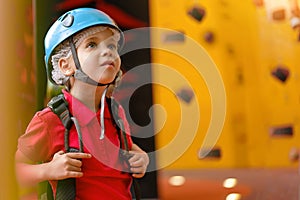 Cute little girl climber in blue protective helmet and gear for climbing standing in climber centre amusement park for children