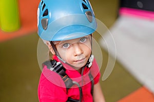 Cute little girl climber in blue protective helmet and gear for climbing standing in climber centre amusement park for children