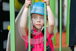 Cute little girl climber in blue protective helmet and gear for climbing standing in climber centre amusement park for children