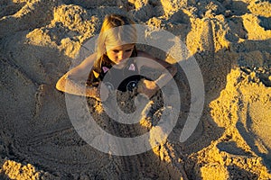 Cute little girl covered with sand. Happy childhood. Relax and play on the beach. Funny kids` activities. Summer concept. Bali,