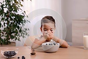 Cute little girl covering her mouth and refusing to eat breakfast at home