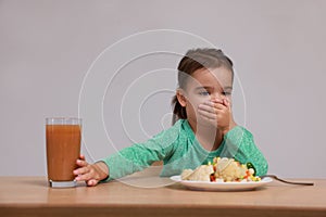 Cute little girl covering mouth and refusing to drink juice at table on grey background