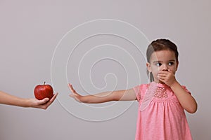 Cute little girl covering mouth and refusing to eat apple on grey background