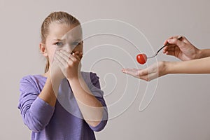 Cute little girl covering mouth and refusing to eat tomato on grey background