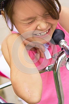 Cute little girl cries sitting on the ground after falling off her bike. Child getting hurt while riding a bicycle.