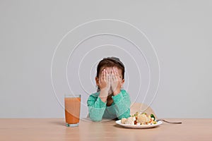 Cute little girl crying and refusing to eat vegetable salad at table on grey background