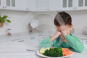 Cute little girl crying and refusing to eat vegetables in kitchen, space for text