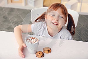 Cute little girl with cup of hot cocoa drink and cookies at home