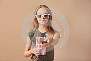 Cute little girl with cup of popcorn switching channels on color background