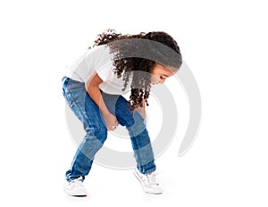 Cute little girl with curls and dark skin bent down to fix shoes