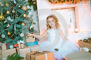 Cute little girl with curly blond hair at home near a Christmas tree