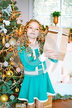 Cute little girl with curly blond hair at home near a Christmas tree with gifts and garlands and a decorated fireplace