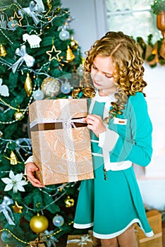 Cute little girl with curly blond hair at home near a Christmas tree with gifts and garlands and a decorated fireplace