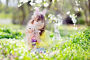 Cute little girl with curly hair wearing bunny ears and summer dress having fun during Easter egg hunt relaxing in the garden