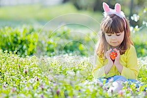 Cute little girl with curly hair wearing bunny ears and summer dress having fun during Easter egg hunt relaxing in the garden