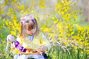 Cute little girl with curly hair wearing bunny ears and summer dress having fun during Easter egg hunt relaxing in the garden