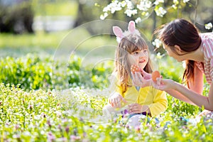 Cute little girl with curly hair wearing bunny ears and summer dress having fun with her young mother, relaxing in the garden