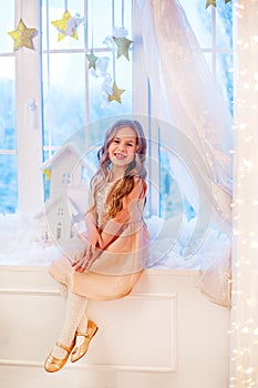 Cute little girl with curly hair at the window in anticipation of Christmas and New Year`s magic