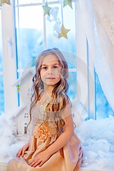 Cute little girl with curly hair at the window in anticipation of Christmas and New Year`s magic