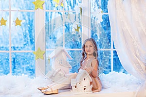 Cute little girl with curly hair at the window in anticipation of Christmas and New Year`s magic