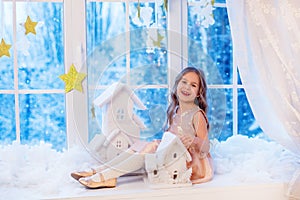 Cute little girl with curly hair at the window in anticipation of Christmas and New Year`s magic