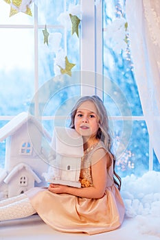 Cute little girl with curly hair at the window in anticipation of Christmas and New Year`s magic