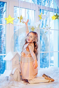 Cute little girl with curly hair at the window in anticipation of Christmas and New Year`s magic