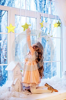 Cute little girl with curly hair at the window in anticipation of Christmas and New Year`s magic