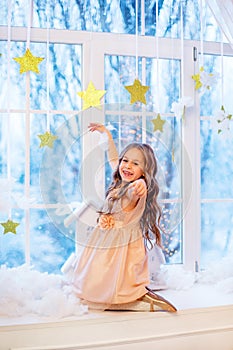 Cute little girl with curly hair at the window in anticipation of Christmas and New Year`s magic