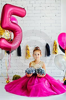 Cute little girl with dark hair, in a beautiful holiday dress and pink balloons for her birthday. The child is 5 years old