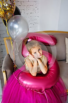 Cute little girl with dark hair, in a fancy dress and balloons for her birthday. Child 5 years old