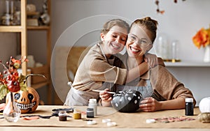 Cute little girl daughter gently hugs mom during painting Halloween pumpkins with mother at home